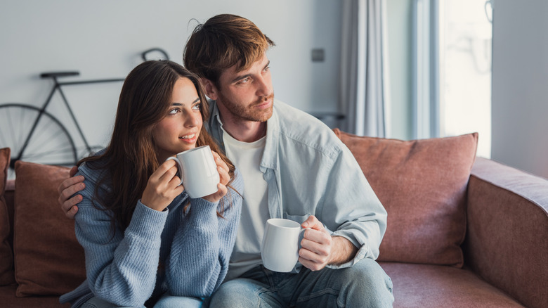 Couple drinking coffee on couch looking out apartment window