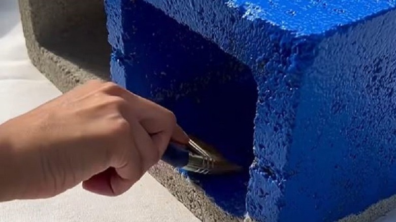 Person painting concrete block blue for shoe storage DIY