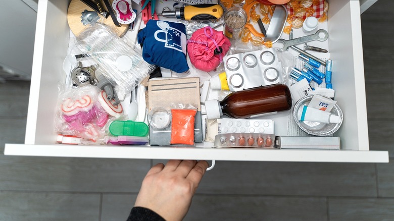 Person opening messy drawer filled with random odds and ends