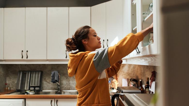 A woman looks through her kitchen cabinet