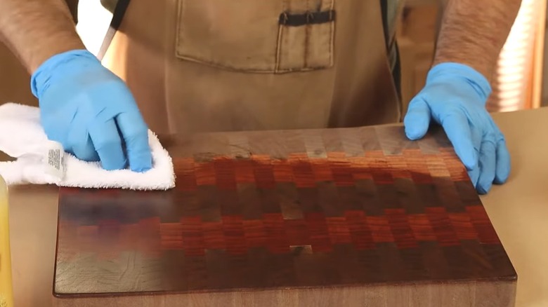 Gloved man adding red-tinted wood finish to cutting board