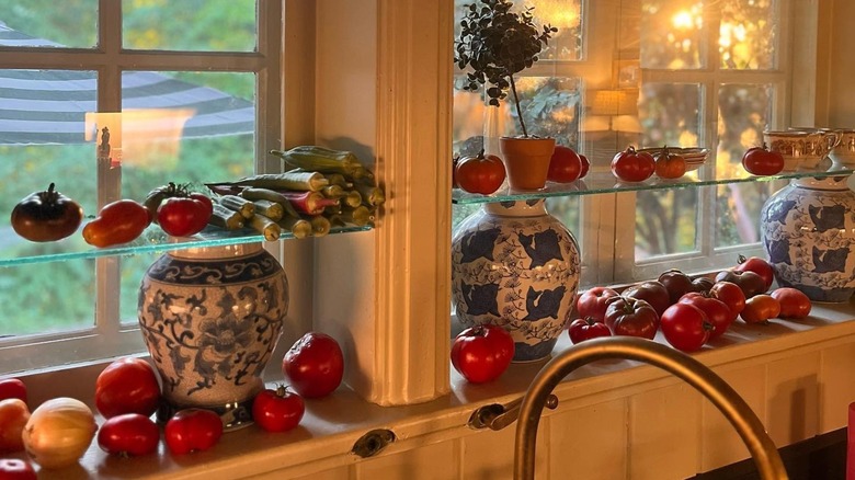 Glass shelves installed in front of kitchen windows, covered in tomatoes and decorative vases