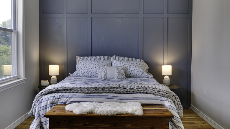 A bed flanked by two table lamps sits in front of a slate blue accent wall