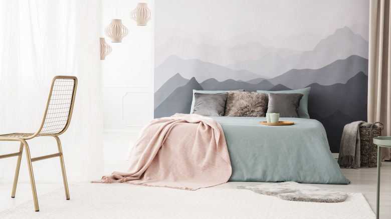 A soft mountain range mural covers the wall behind a bed