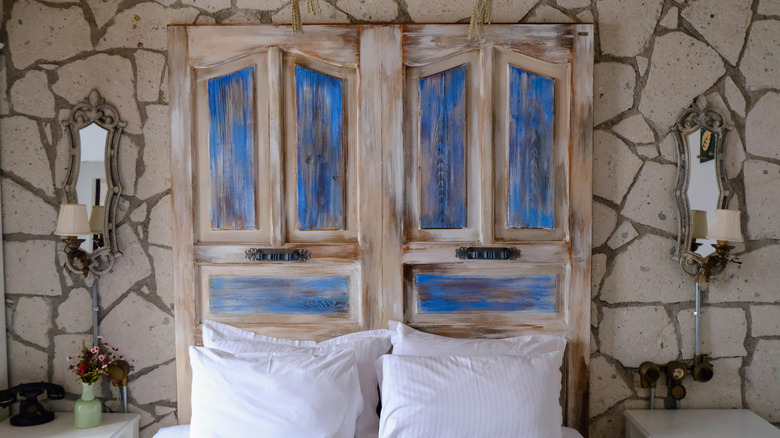 Two aged blue and white doors are against the wall behind a bed