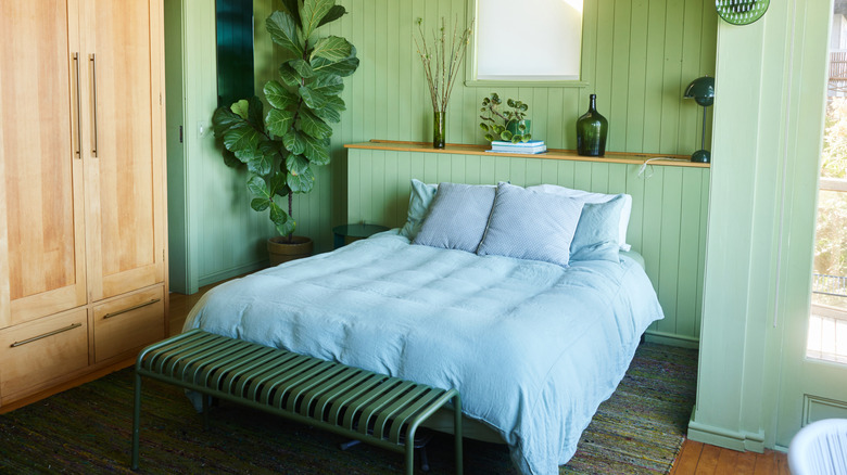 A built-in shelf functions as a headboard in a light green bedroom