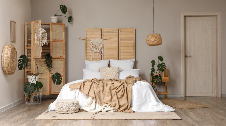 A wooden folding screen divider positioned behind a bohemian bed