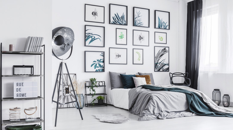 Framed prints hang on a gallery wall behind a bed