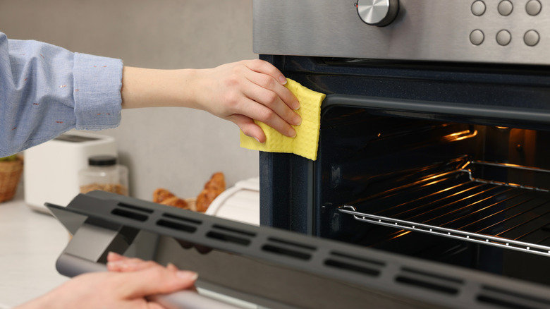Person wiping the interior of an oven with a yellow cloth