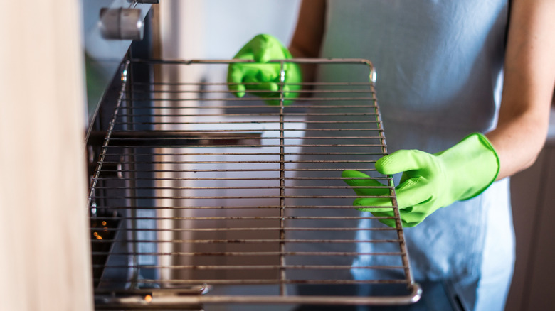 Green gloved hands removing dirty oven racks