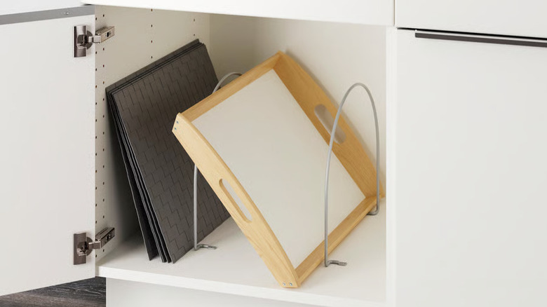An open kitchen cabinet with trays and placemats organized using partition arches