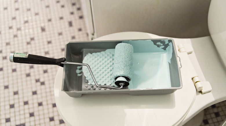 Roller brush in paint tray sitting on toilet lid
