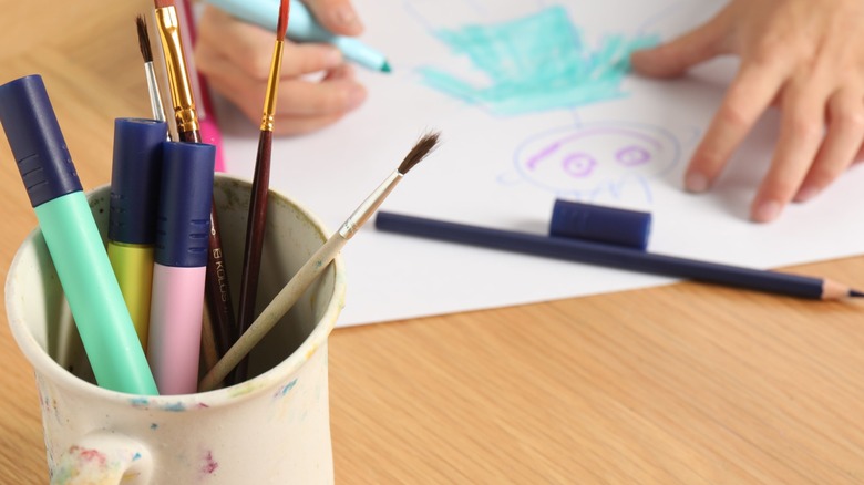 Child drawing near a pencil with that holds markers and paintbrushes.