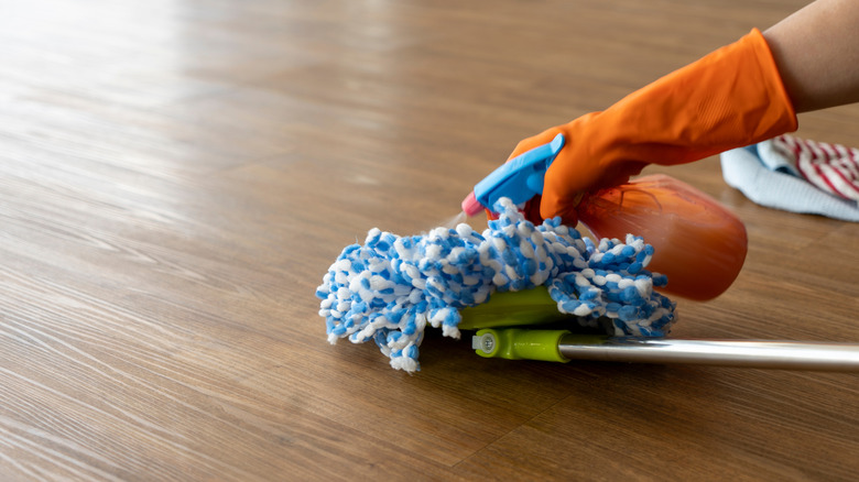 A person wearing orange gloves cleaning a vinyl floors using a sweeper