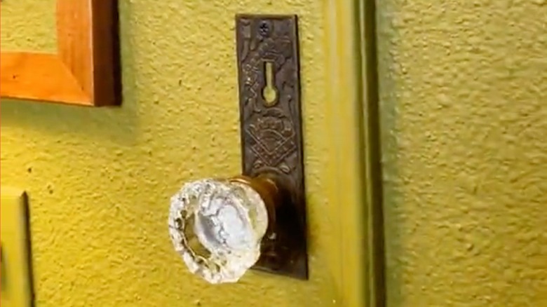 A vintage crystal doorknob mounted on a green bathroom wall