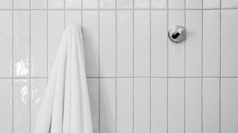 Two chrome hooks on tiled bathroom wall, one with a towel hanging on it