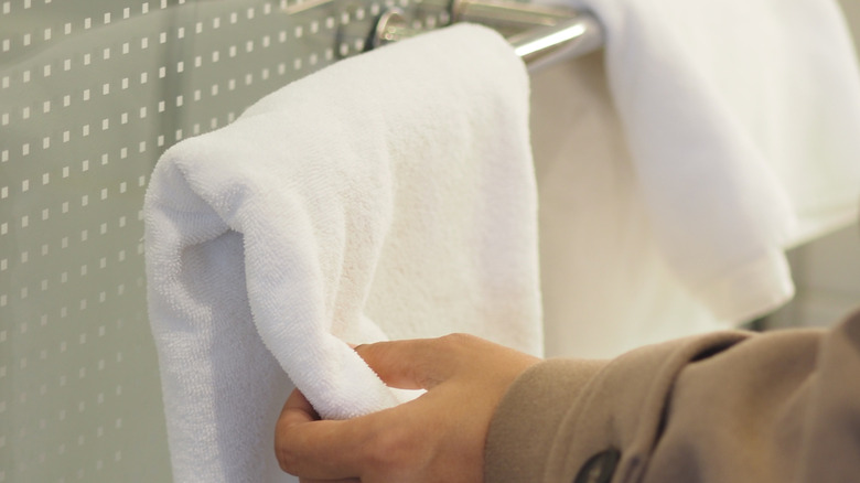 Person reaching for a white towel on a towel bar