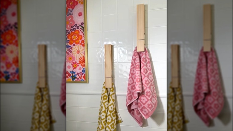 Giant clothespin towel holders hanging on a bathroom wall with colorful towels clipped in them