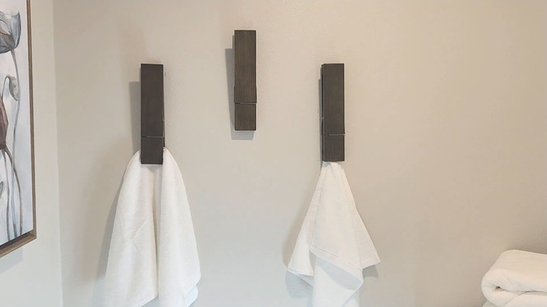 Three giant clothespin towel holders on the wall with white towels in two of them