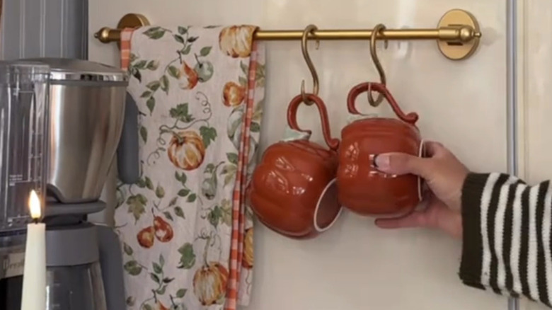 Person hanging a pumpkin mug on a hook along with a towel on a magnetic towel bar