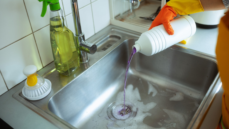 Person pouring purple liquid down a kitchen sink