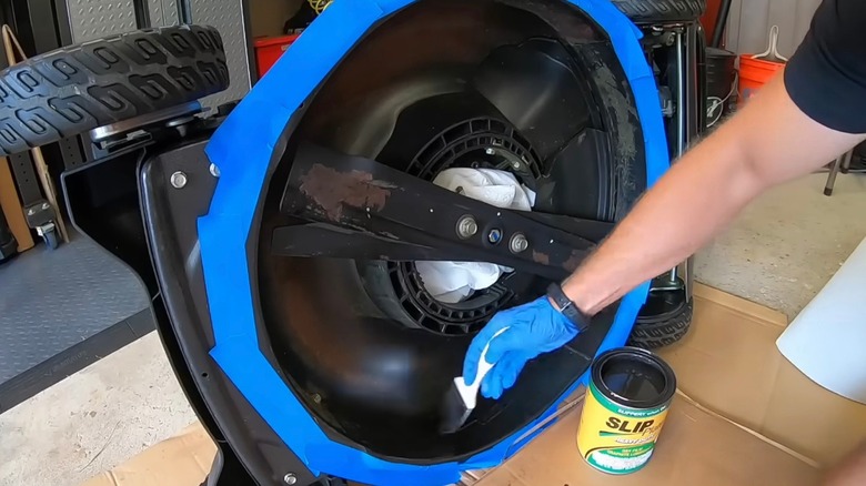 Homeowner applying lubricant to lawn mower deck