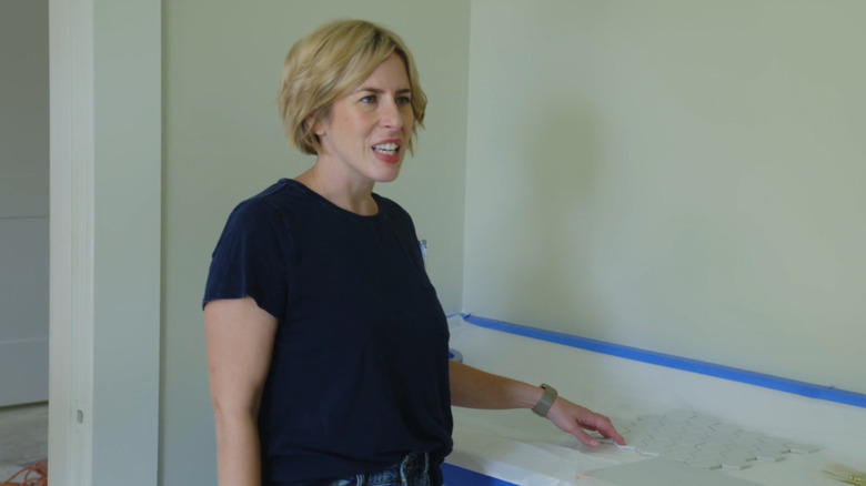 Erin Napier, a woman with short cropped blonde hair, in a room pointing at some laid out tiles