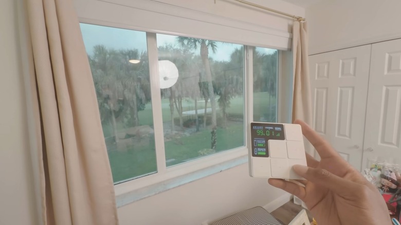 Hand holding a white remote and controlling the shades over a window