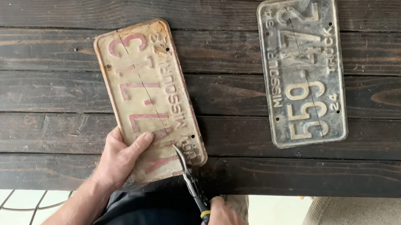 Hands cutting license plate over a wooden table