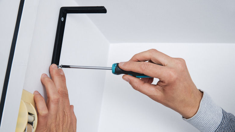 A person mounting a shelf bracket on the wall
