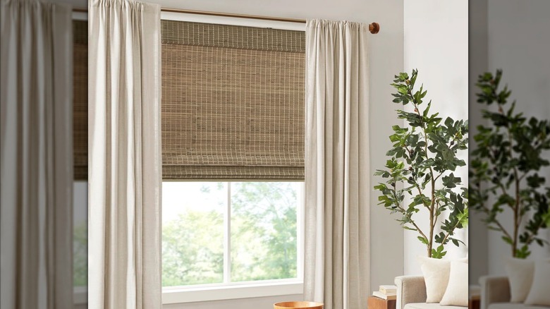 Dark woven wood bamboo shades paired with beige curtains and rich wood furniture