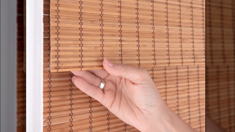 Woman with wedding ring holding tightly woven bamboo wood shade