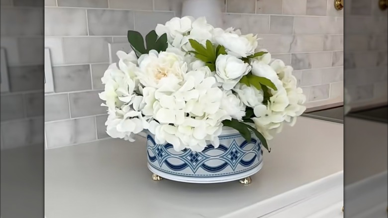 White flowers are arranged in a cookie tin decorated with blue ribbon