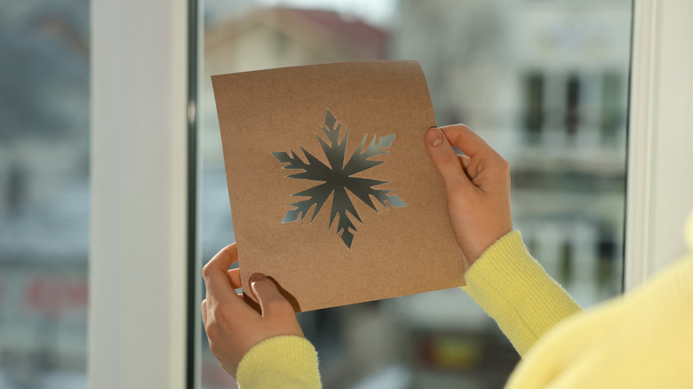 person holding snowflake stencil in front of window