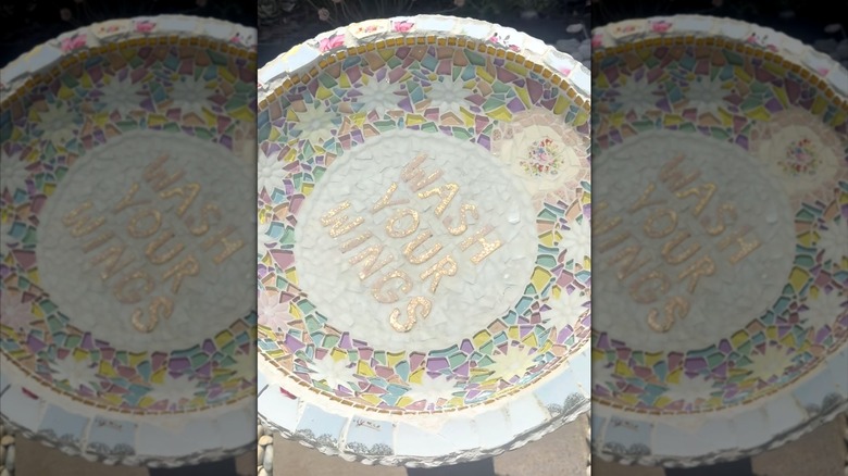 a colorful mosaic birdbath inlayed with handmade letters reading "Wash Your Wings"