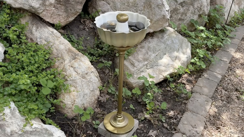 A birdbath made from a Bundt pan and a brass stand.