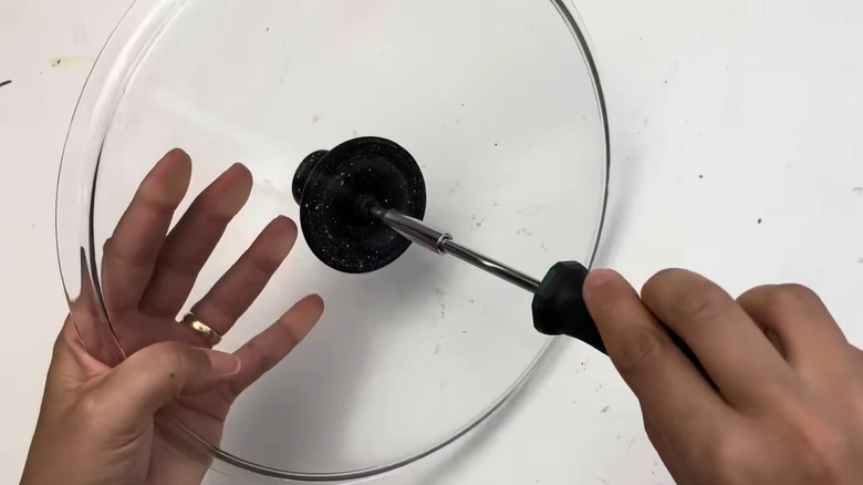Person removing the handle from an old pot lid