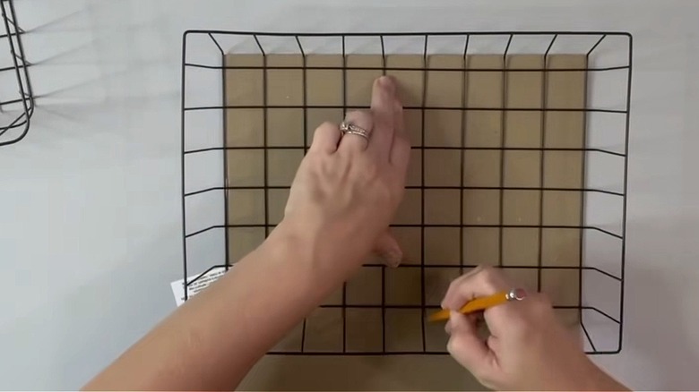 Person holding black wire basket and pencil on a gray table