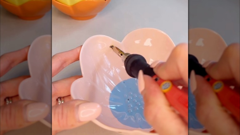 A person uses a soldering iron to create holes in a fluted plastic bowl