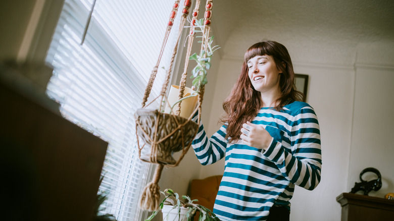 A woman smiles while watering a hanging houseplant