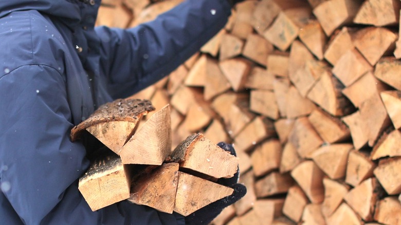 Person pulling an armload of firewood from a large outdoor stack