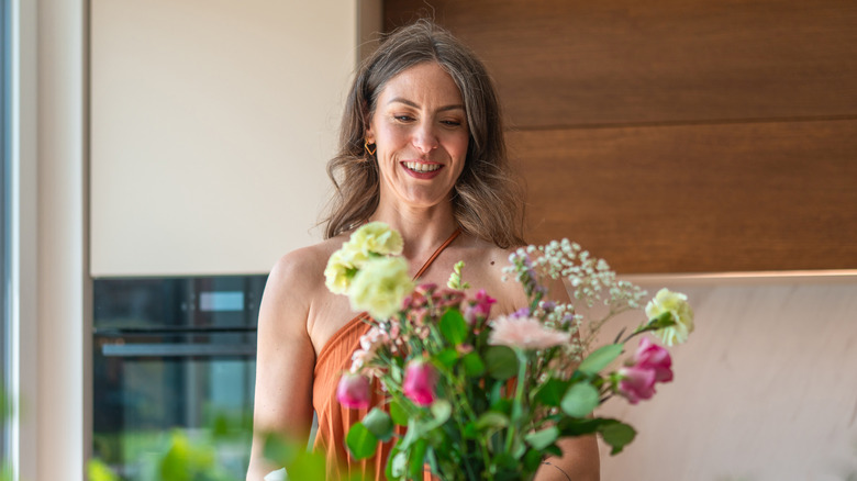 A woman looks at a bouquet of flowers in a kitchen