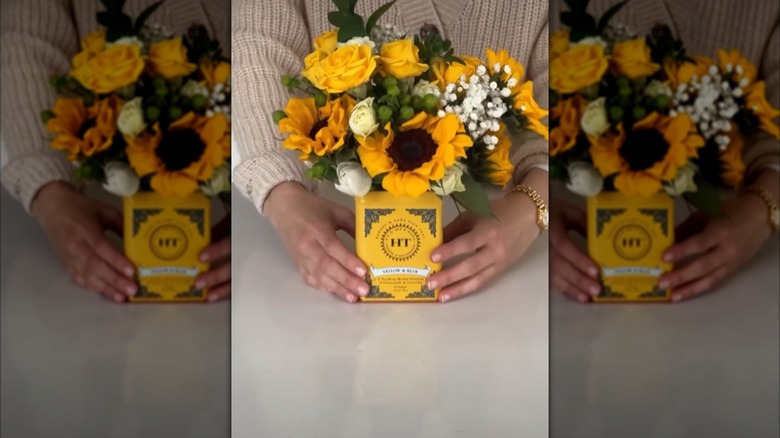 A woman holding a yellow tea tin full of yellow and white flowers