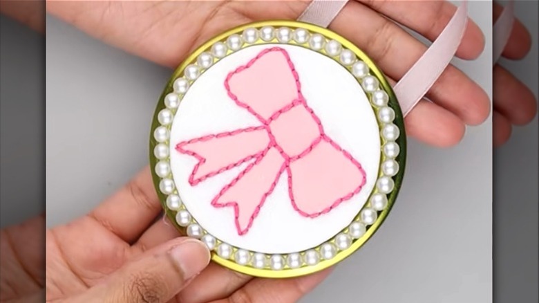 Creator holding a DIY wall decor piece featuring a pink bow made on a jar lid