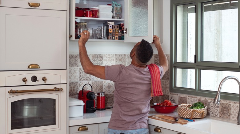 Man looking for items in filled kitchen wall cabinet