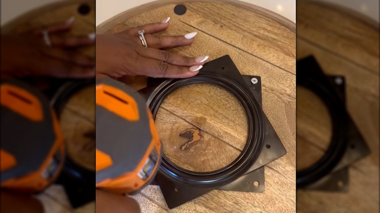 Person holding turntable hardware while screwing it to a round wooden tray