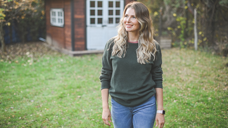 A woman smiles and stands on a patchy lawn
