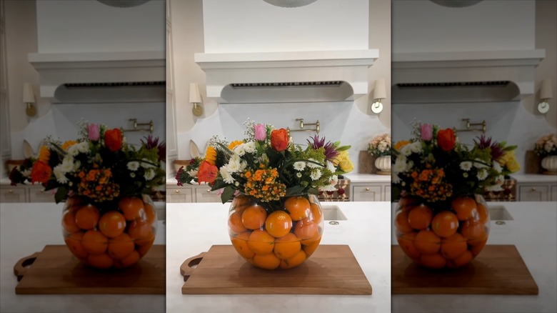 Oranges filling up a large clear bowl with flowers on top.