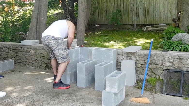 Man assembling a DIY outdoor grill from concrete cinder blocks