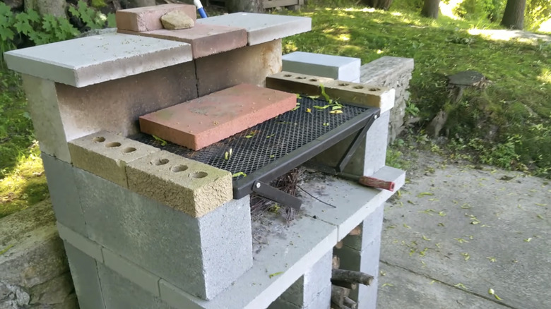 A DIY concrete block outdoor grill sits on a backyard patio